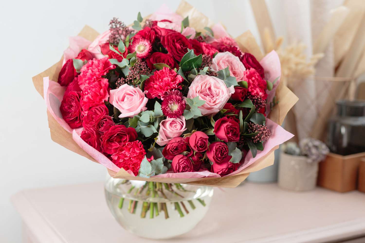 Close-up beautiful luxury bouquet of mixed red and pink flowers in glass vases. the work of the florist at a flower shop. Wallpaper Romance in Bloom Bouquet with red roses, pink garden roses, carnations, eucalyptus in a glass vase—ideal for Valentine’s Day or any special occasion